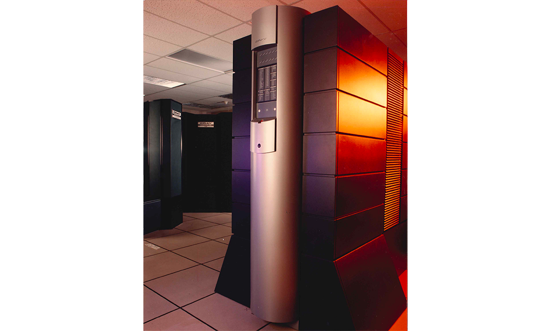 ASA's tall, dark gray Cray C90 supercomputer tower with a prominent silver vertical pillar in the foreground, with the older Cray X-MP system visible in the server room background