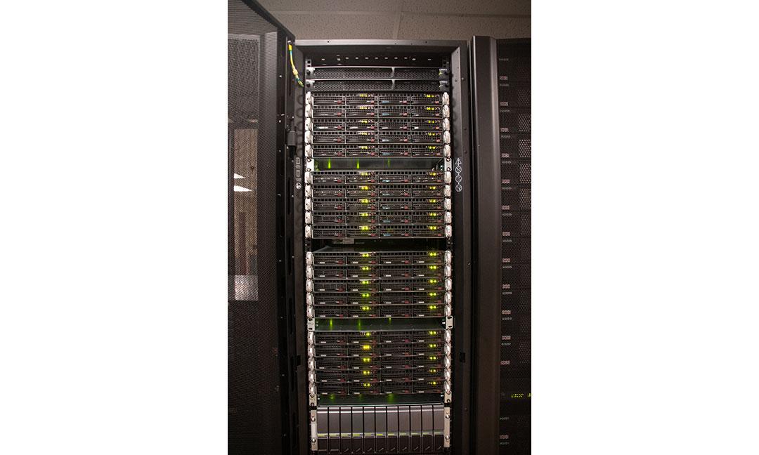 Front view of tall black supercomputer rack with door open to showcase multiple computing nodes with multicolored led lights